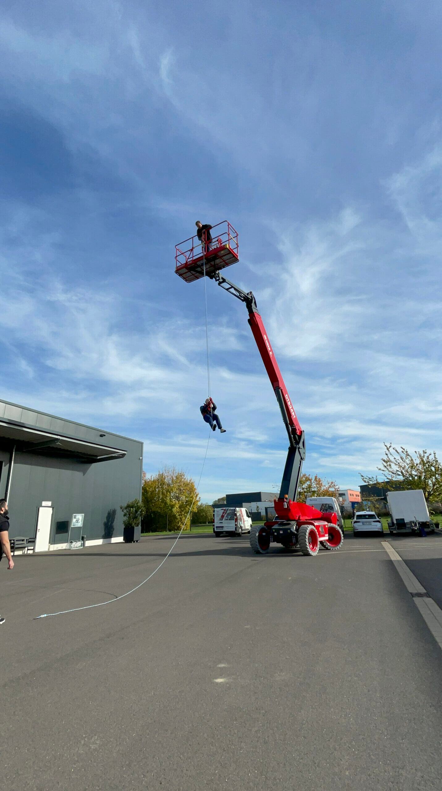 Mehrere Arbeiter mit gelben Warnwesten bedienen Gabelstapler und rote Teleskoplader, bewegen Holzpaletten vor Industriehalle.