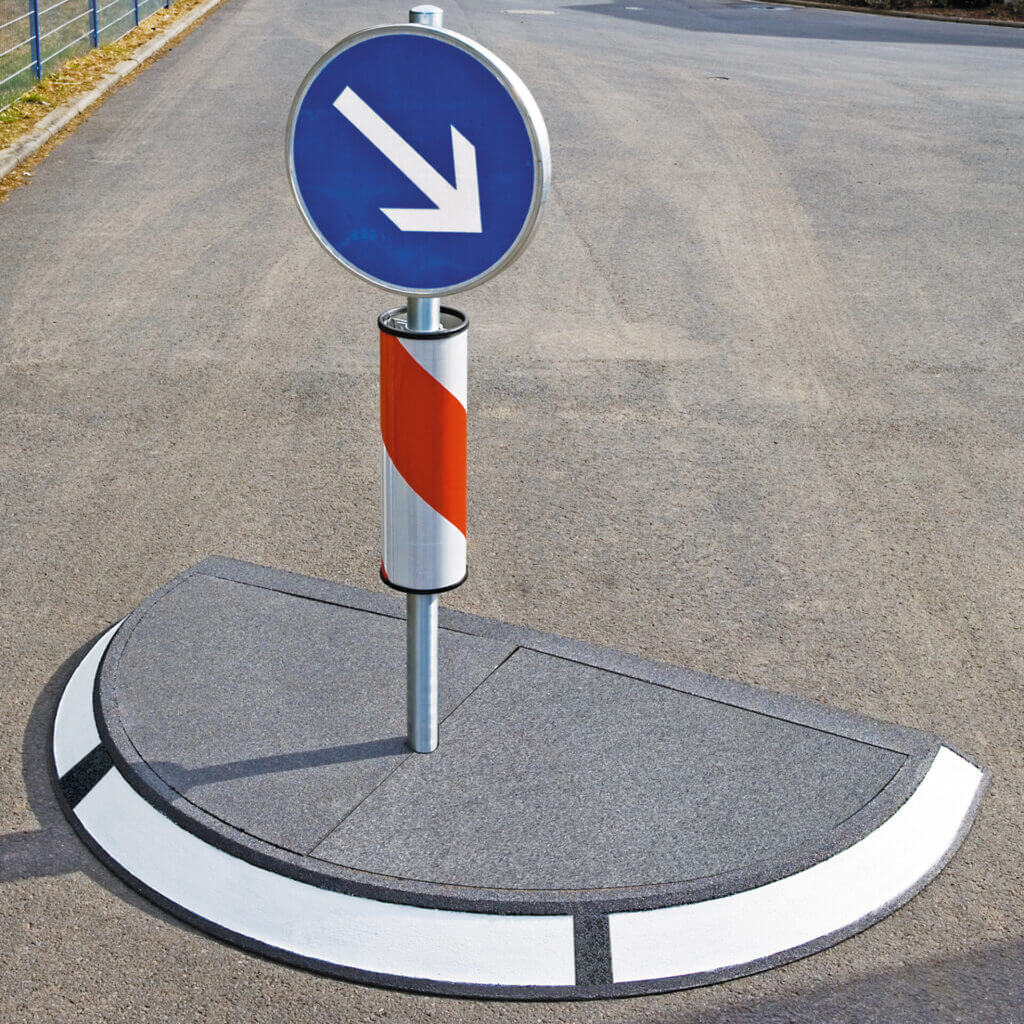 Verkehrsinsel mit blauem Schild und weißem Links-Pfeil, Pfosten mit rot-weißen Streifen, auf Gehwegmitte im Straßenverkehr.