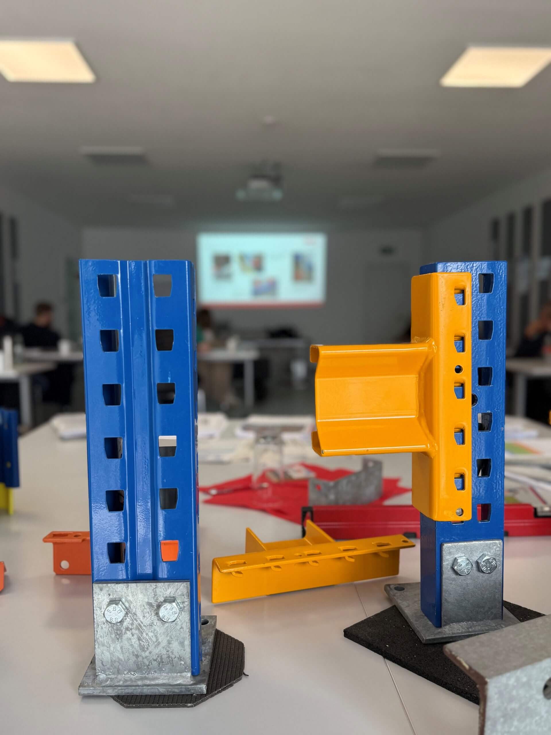 Ein Gabelstapler transportiert Holzpaletten vor einem Lagerhaus, mehrere Personen mit Warnwesten beobachten bei klarem Wetter.