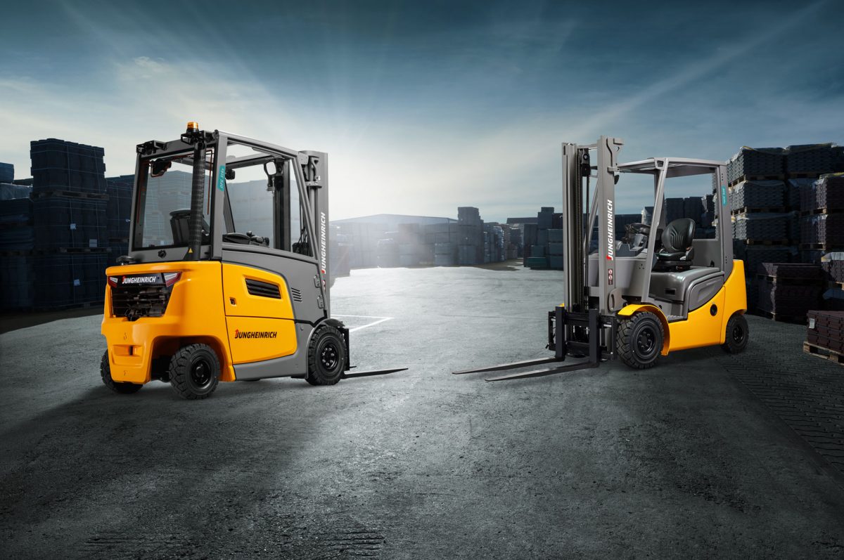 Zwei gelb-graue Jungheinrich Gabelstapler stehen auf Industriegelände, im Hintergrund Palettenstapel und bewölkter Himmel.