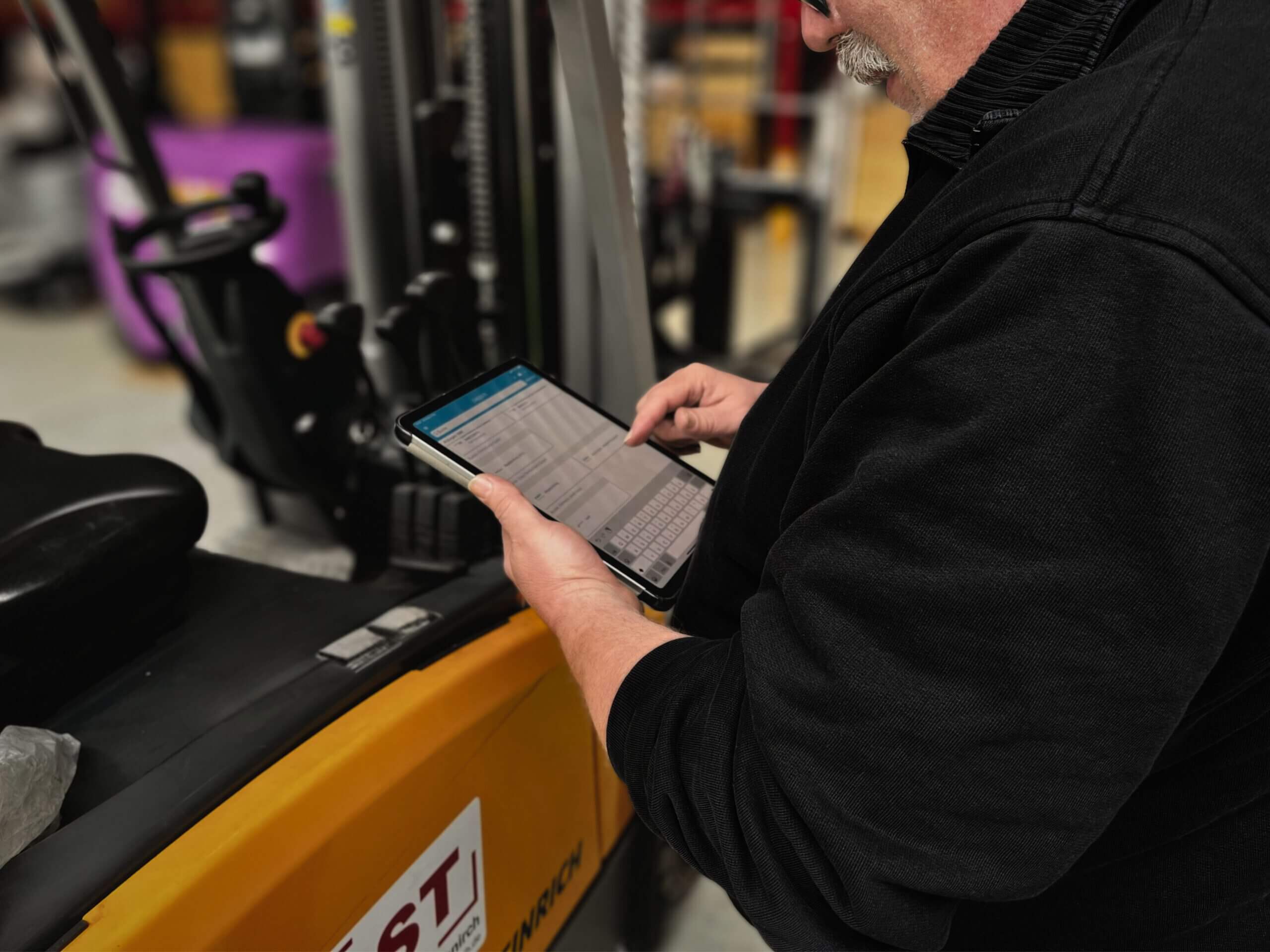 Eine Person mit Handschuhen montiert oder entfernt eine gelbe Zylinderbürste aus einer Bodenreinigungsmaschine.