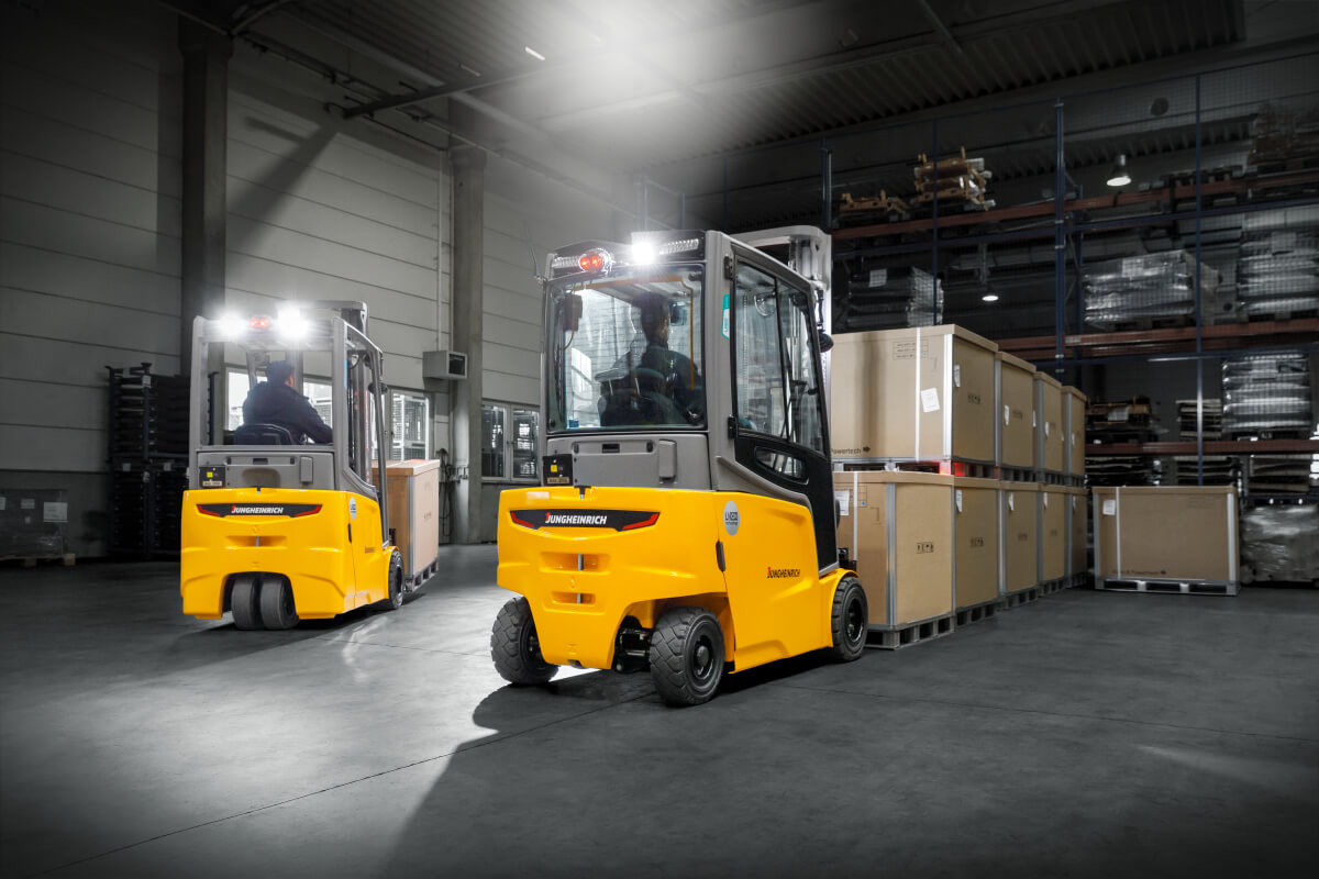 Zwei gelb-graue Jungheinrich Gabelstapler stehen auf Industriegelände, im Hintergrund Palettenstapel und bewölkter Himmel.