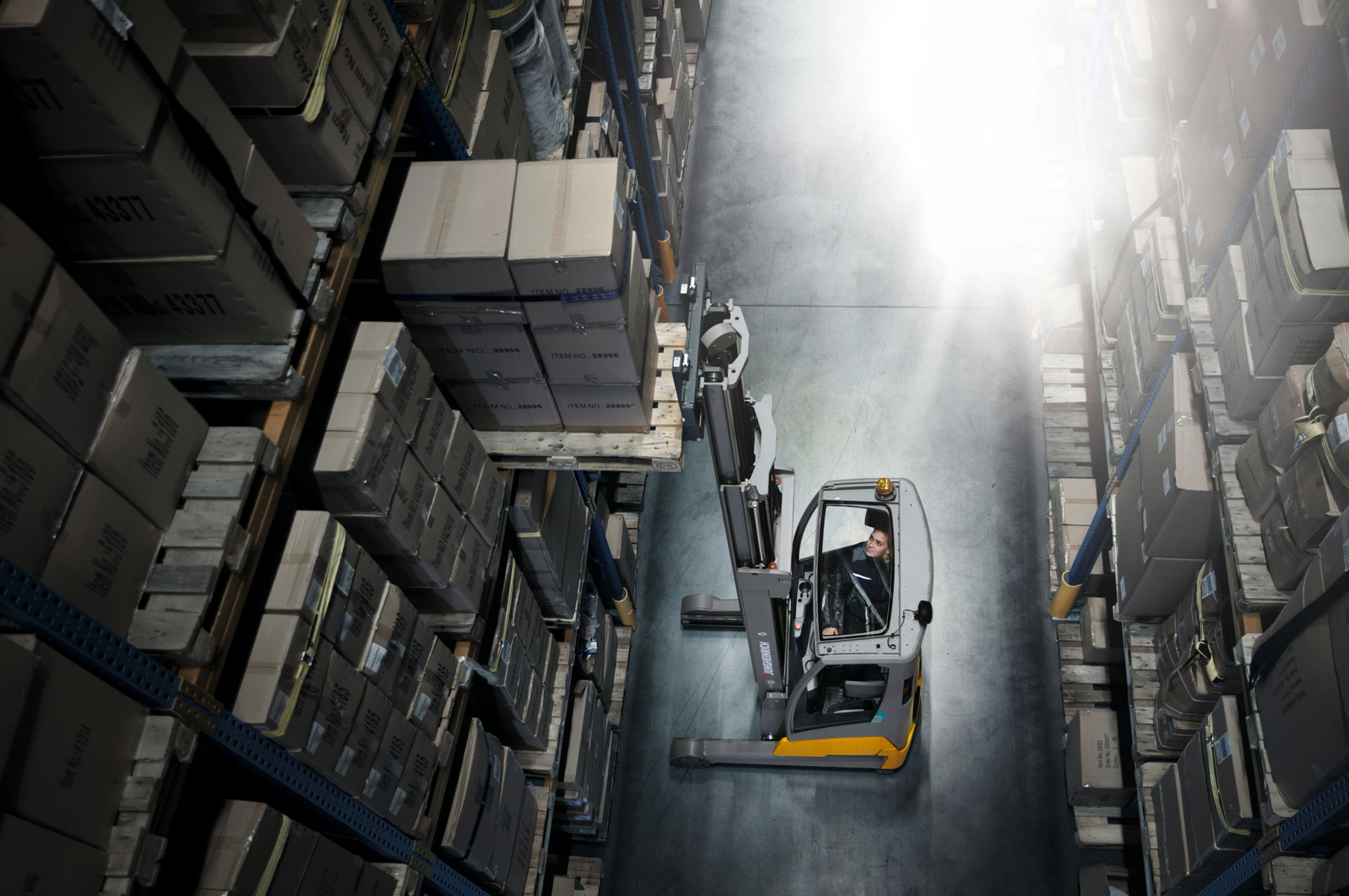 Ein Mann bedient einen Gabelstapler und hebt Kartons in einem Lagergang mit Regalen voller Kisten und Kartonboxen auf.