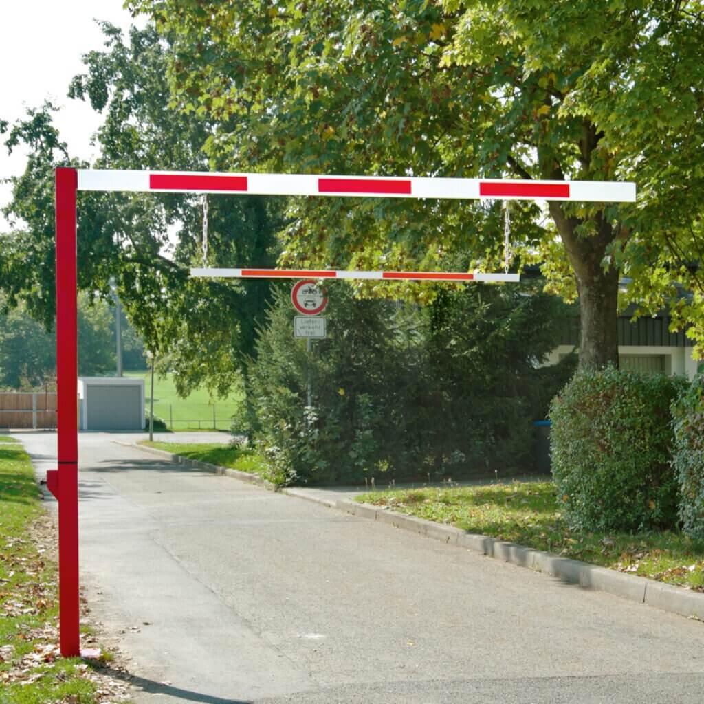 Rot-weißer Durchfahrtbegrenzer über geteerten Straße, seitlich Bäume und Büsche, Verkehrsschild für Höhenbegrenzung.