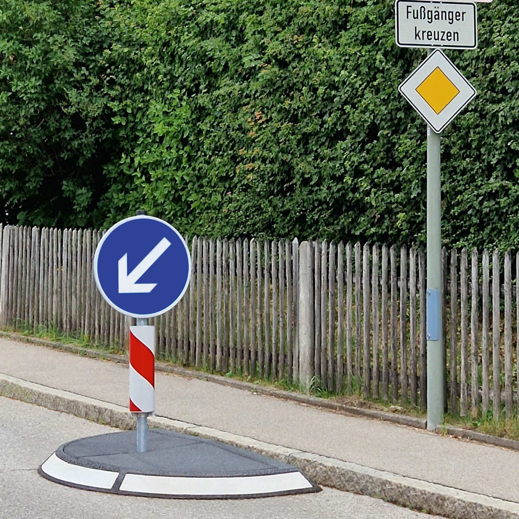 Verkehrsinsel, halbrund, Fahrbahnverengung, mit nach links weisendem Pfeil.