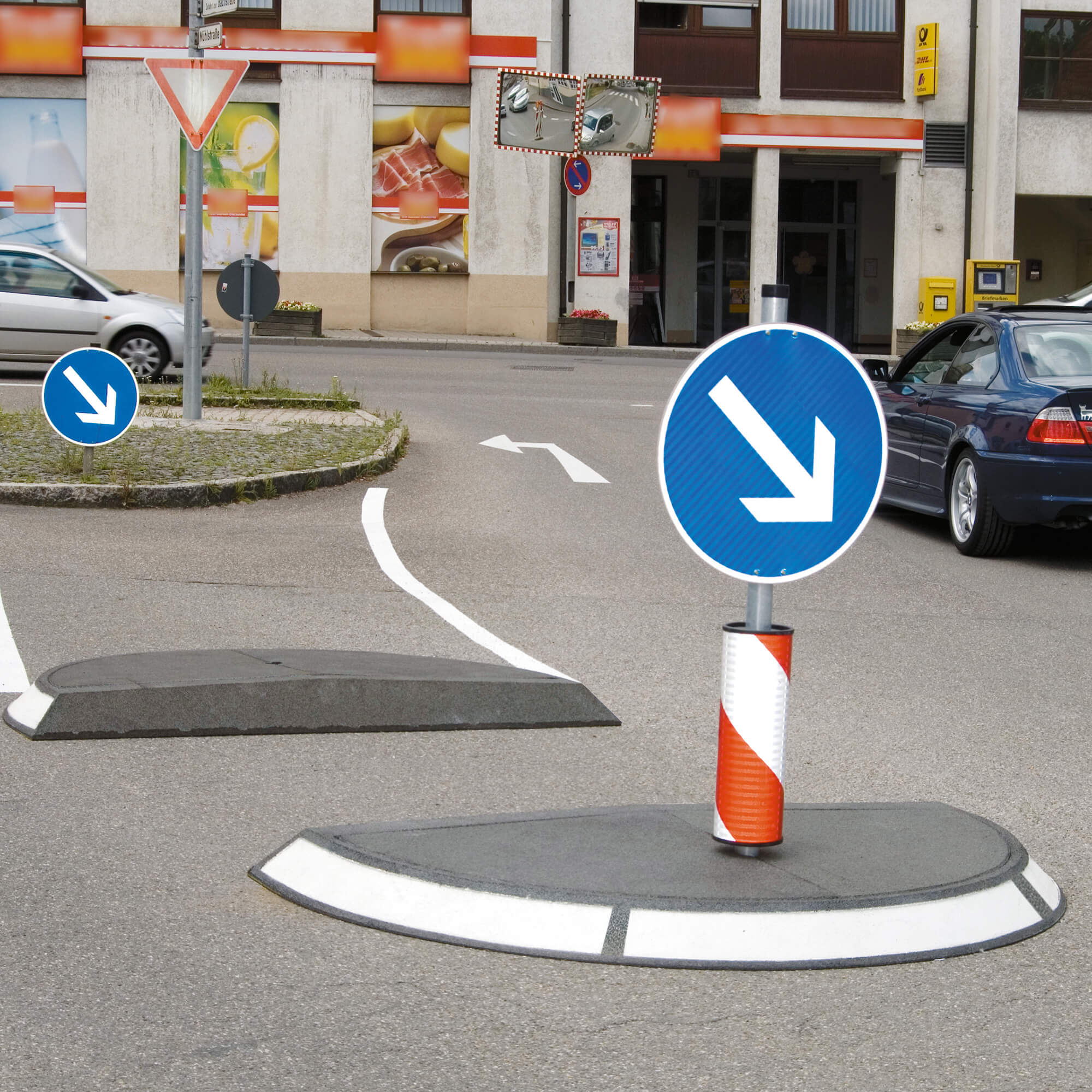 Verkehrsinsel, genutzt als Straßenquerung ,it nach rechts weisendem Pfeil und Warnsockel in rot weiß.