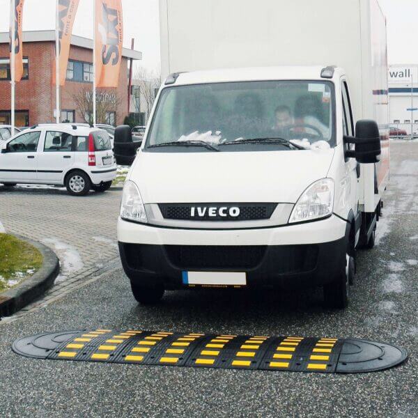Weißer Iveco Lieferwagen mit SafeRide-System nähert sich gelb-schwarzer Bodenschwelle auf nasser Straße in der Stadt.