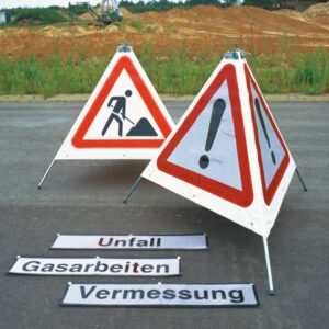 Zwei dreieckige Verkehrsschilder: Warnschild mit Ausrufezeichen, Baustellen-Symbol, daneben deutsche Hinweis-Banner am Boden.