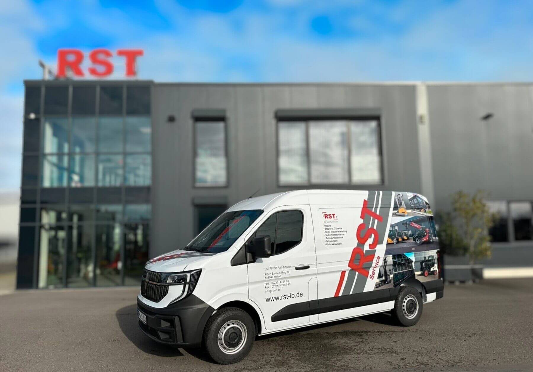 Weißer RST Transporter vor modernem grauen Gebäude mit großen Fenstern und rotem RST Logo auf dem Dach geparkt.