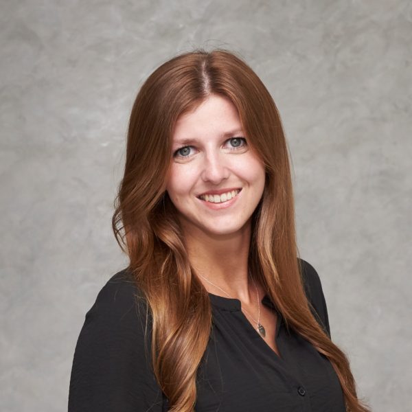 Mann mit kurzem grauem Haar lächelt, trägt dunkles Hemd vor hellem Hintergrund; Porträt für Technische Industrieberatung.